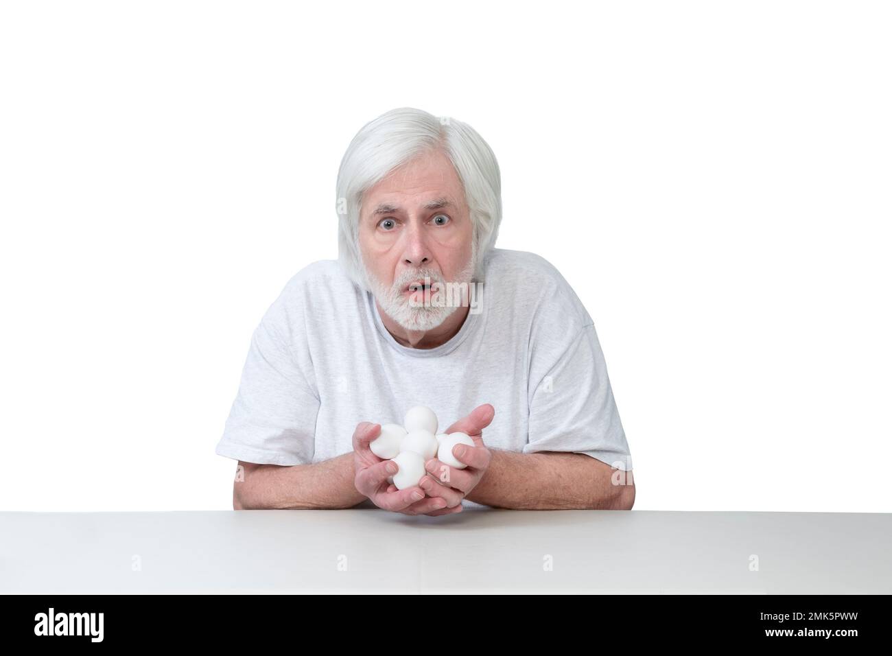 Colpo orizzontale di un vecchio seduto a un tavolo con le mani piene di uova che si guarda molto sorpreso o spaventato. Isolato su bianco. Molte copie Foto Stock
