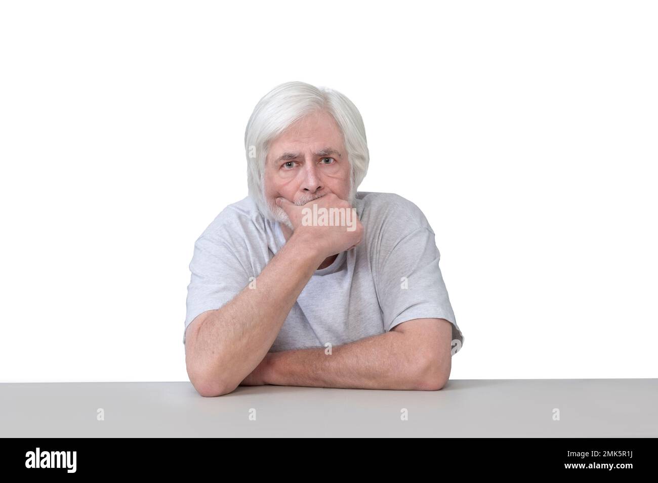 Scatto orizzontale di un vecchio seduto a un tavolo con la mano al mento nel profondo del pensiero. Isolato su bianco. Molto spazio di copia. Foto Stock