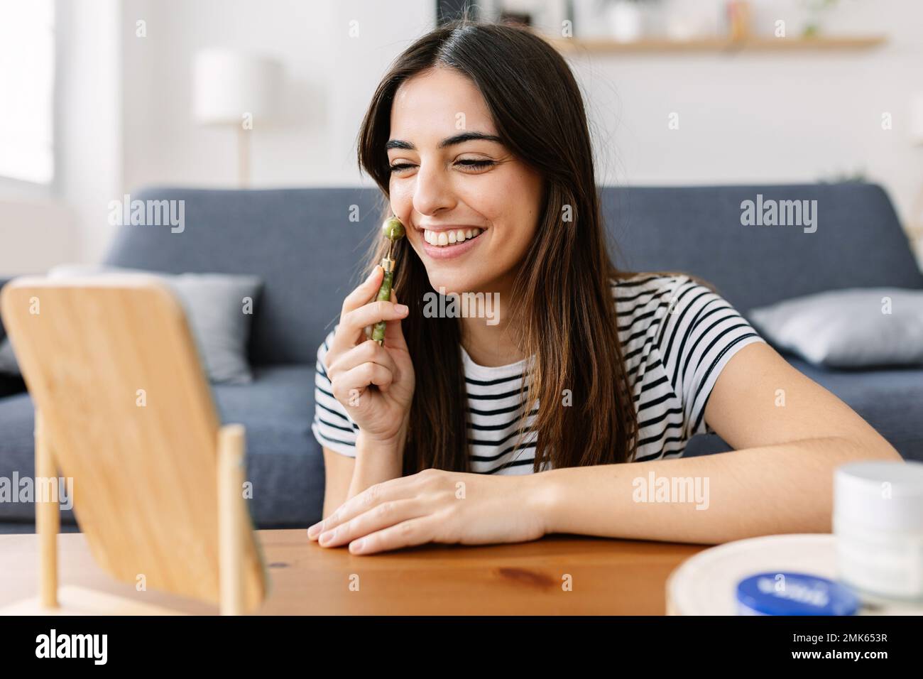 Felice giovane donna che usa il rullo di giada viso naturale sulla guancia Foto Stock