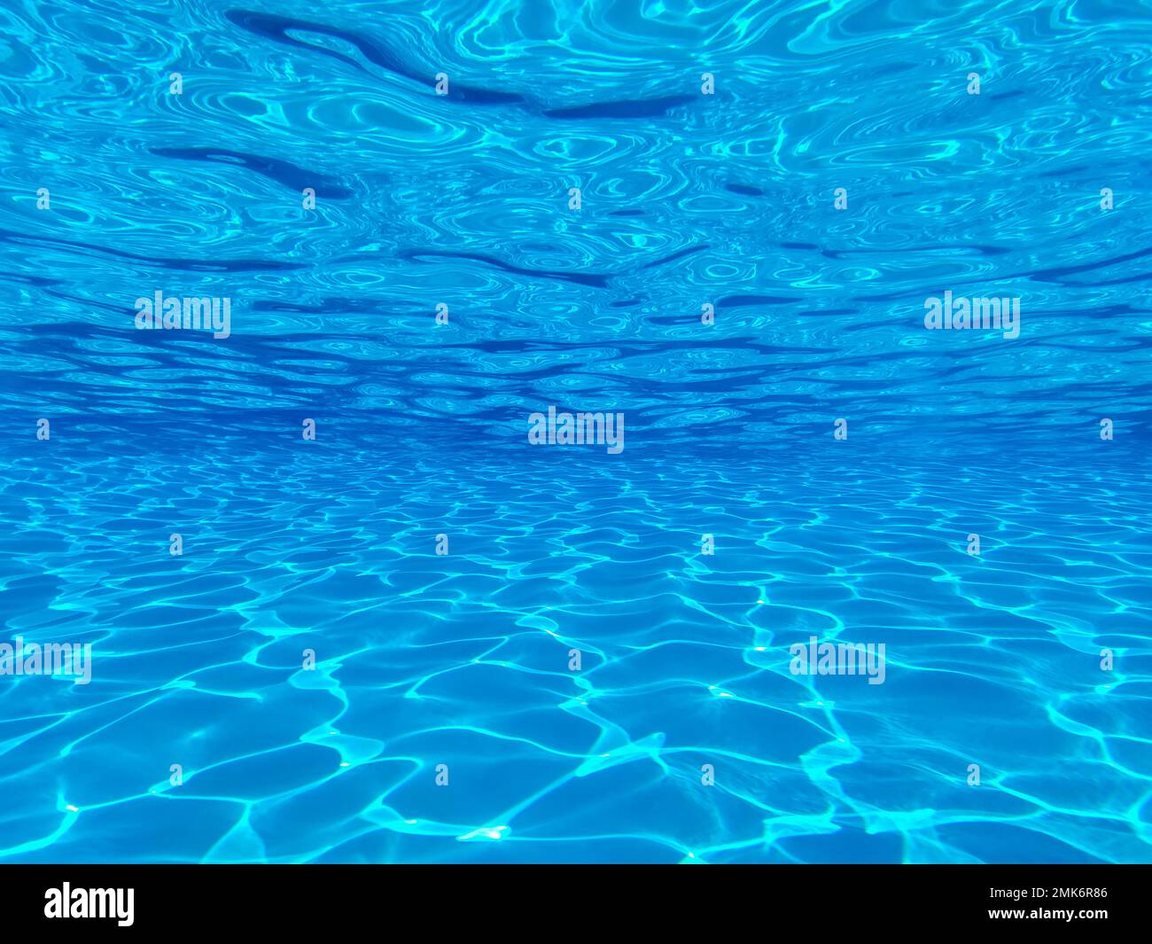 La vista attraverso un porto panoramico tra il pavimento, il fondo e la superficie della lussuosa piscina e l'acqua blu con riflessi del sole presso il resort Foto Stock