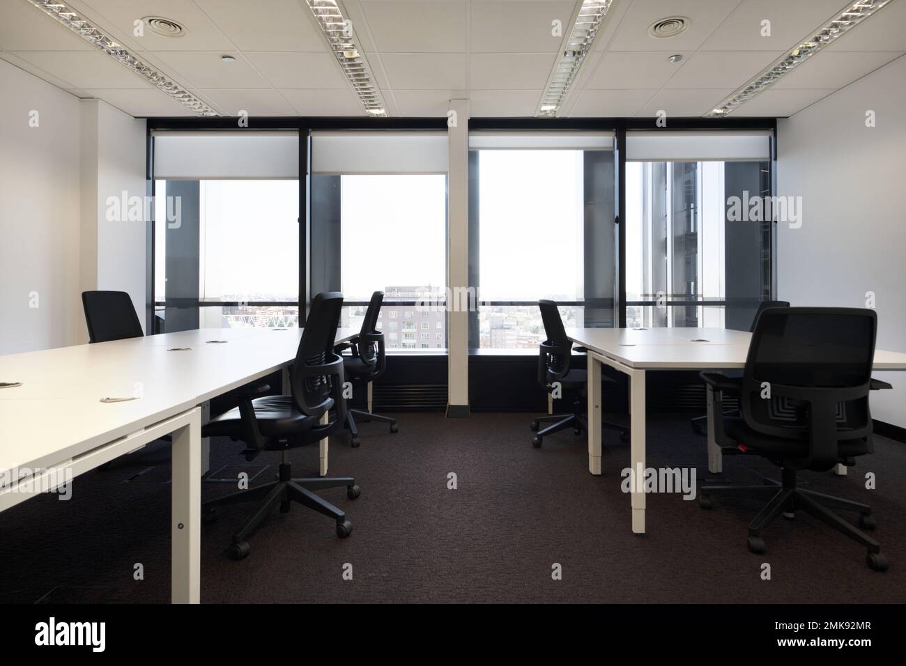 Tavoli da ufficio con sedie girevoli nere in un ufficio con finestre che si affacciano sulla città Foto Stock