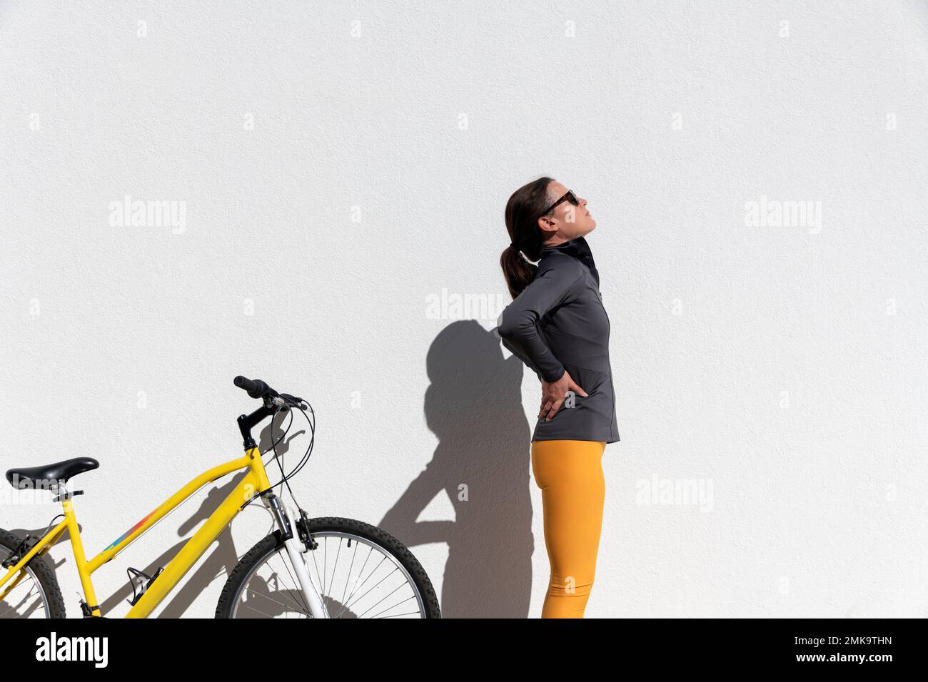 ciclista donna con dolore lombare in piedi accanto alla bici che tiene e massaggiare il suo crampo nella colonna vertebrale e nel muscolo. Spazio di copia Foto Stock