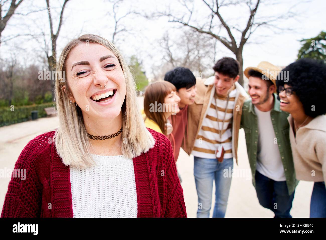 Giovane ragazza sorridente che guarda la fotocamera all'aperto con un gruppo di amici. Persone felici divertirsi insieme concentrarsi su una bella giovane donna. Università Foto Stock