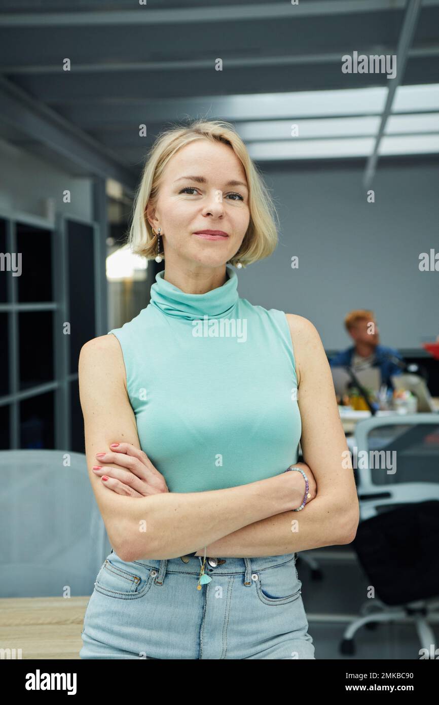 Verticale sicuro donna di affari caucasica che guarda la macchina fotografica in piedi con le braccia incrociate in ufficio. Foto Stock
