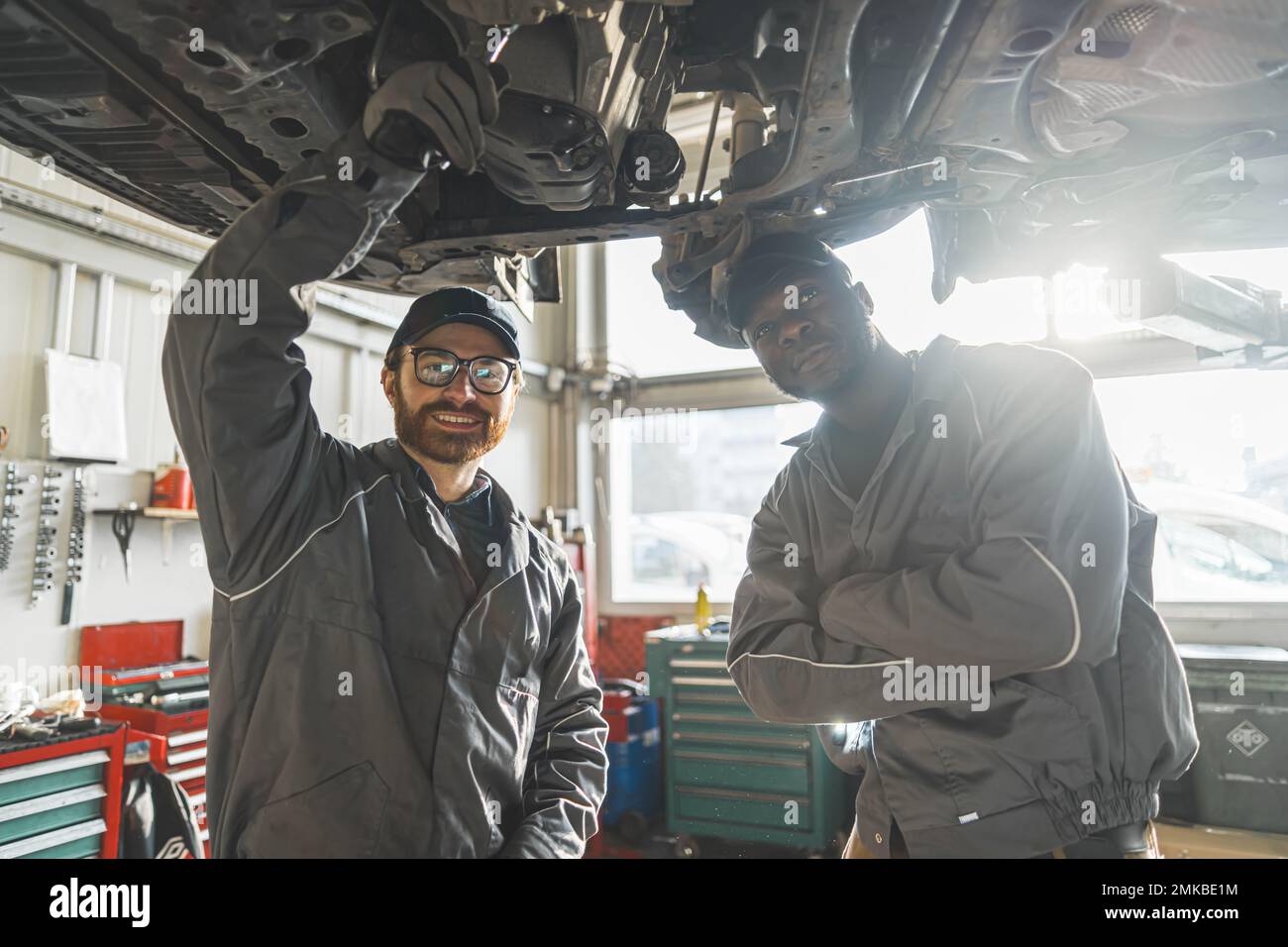 Due meccanici che indossano uniformi in un'officina di riparazione di automobili che si posano sotto un'auto su un ascensore. Foto di alta qualità Foto Stock