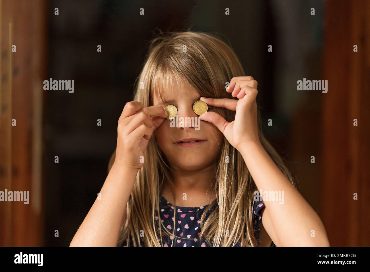 Giovane ragazza sorridente che tiene monete da 20 cent al posto dei suoi occhi. Foto Stock