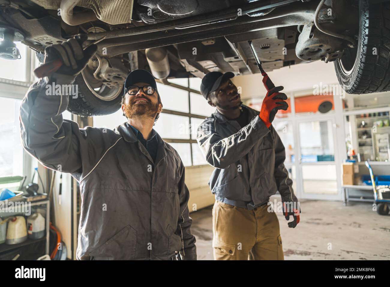 Due meccanici che lavorano sotto un'auto sollevata utilizzando attrezzi in un moderno negozio di riparazione auto. Foto di alta qualità Foto Stock