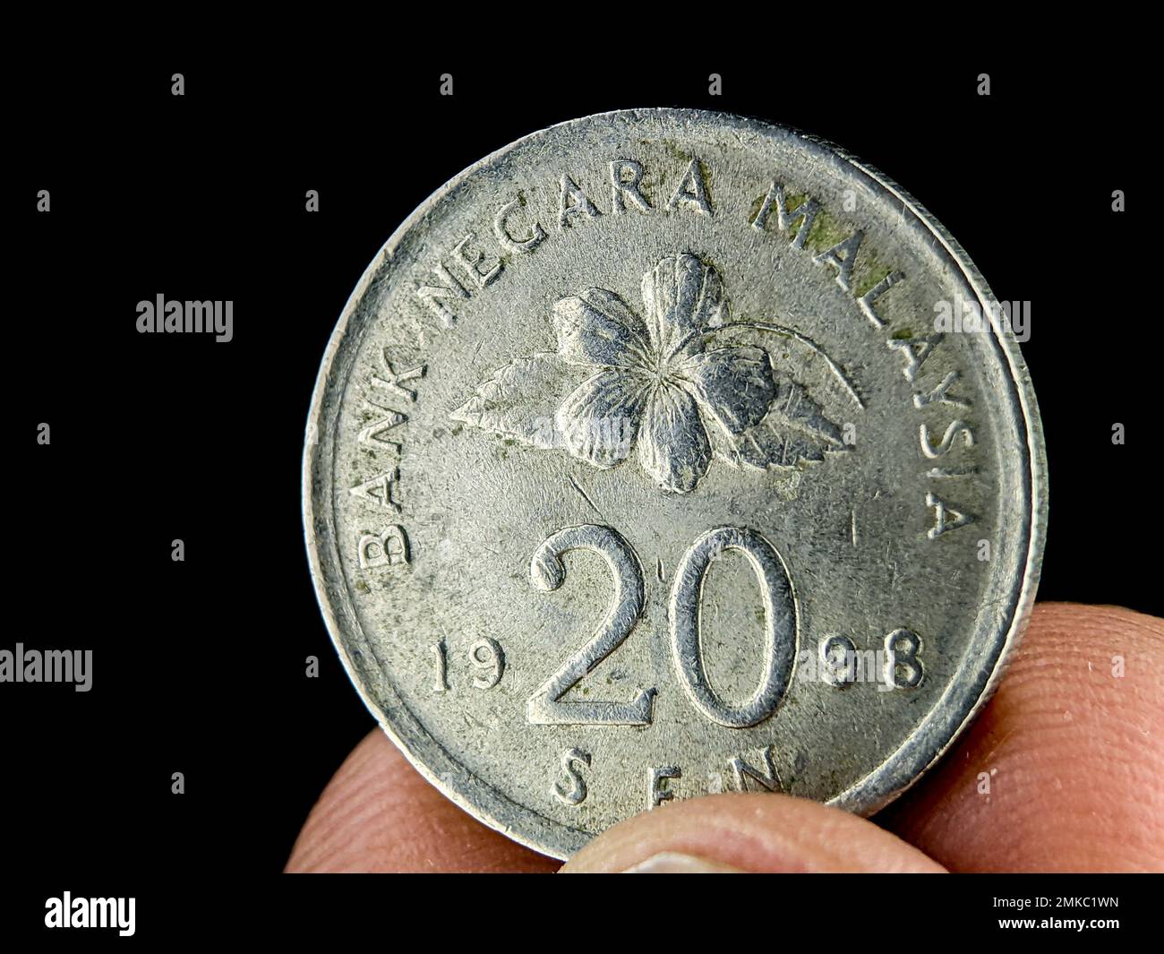 Dito di primo piano che tiene la vecchia moneta malese da 20 cent su sfondo nero. Foto Stock
