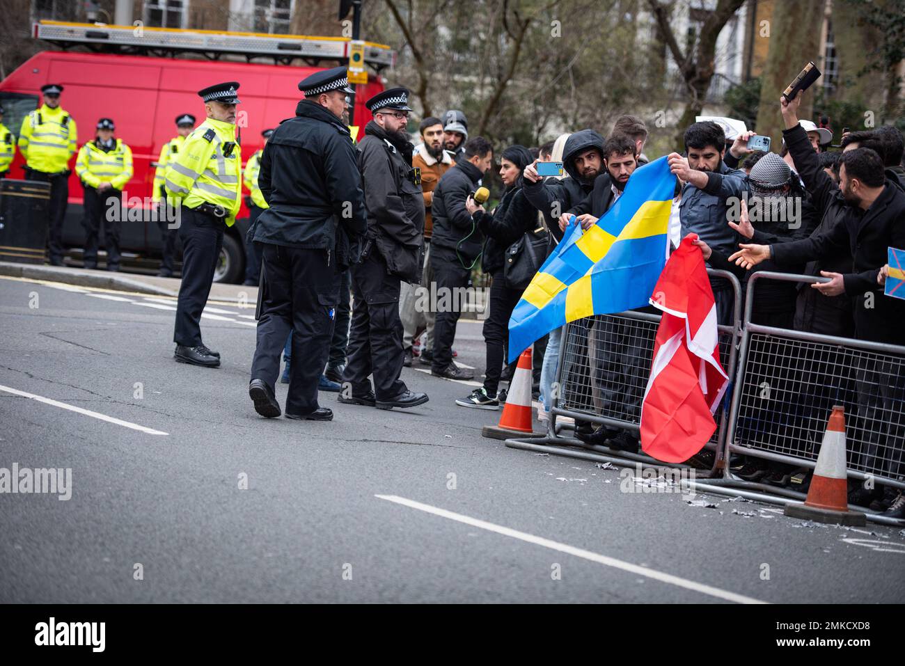 La polizia metropolitana è in guardia mentre i manifestanti si preparano a bruciare le bandiere svedesi e danesi durante la manifestazione contro il Corano Burning in Svezia. L’alto rappresentante dell’Alleanza delle civiltà delle Nazioni Unite ha condannato l’incendio del libro sacro musulmano da parte di un politico di estrema destra svedese-danese come un “atto vile”. Rasmus Paludan, leader del partito politico danese di estrema destra Hard Line, ha effettuato la stunt al di fuori dell'ambasciata turca in Svezia sotto la protezione della polizia locale venerdì 27 gennaio 2023. Foto Stock