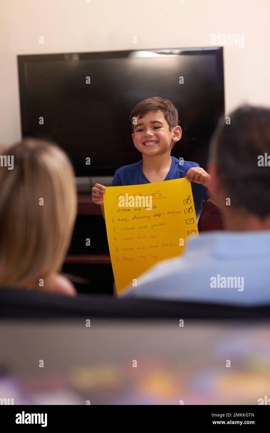 Ive ha finito le mie faccende. un ragazzino che mostra ai suoi genitori una lista di chore a casa. Foto Stock