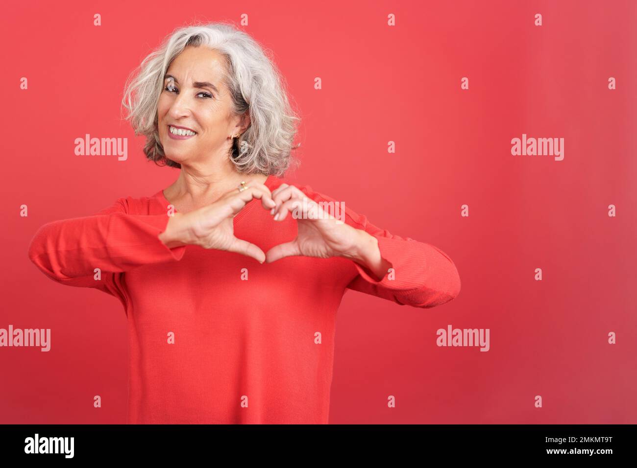Donna matura che rappresenta un cuore a forma di dita Foto Stock