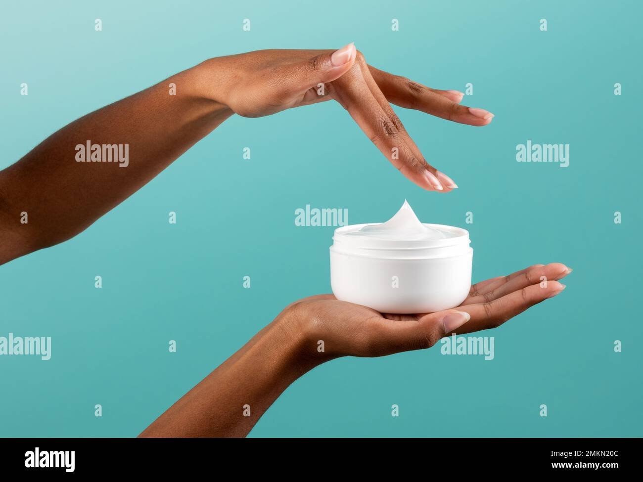 Crop African American femmina prendendo crema corpo da vaso bianco durante la routine di cura della pelle contro sfondo turchese Foto Stock