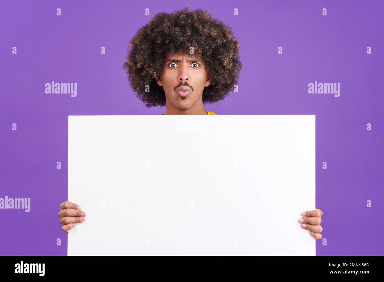 Uomo africano sorpreso con capelli ricci che tiene un pannello vuoto Foto Stock