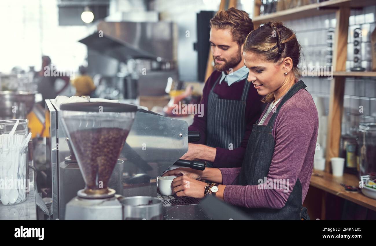 Conoscere la loro strada intorno a una macchina da caffè. due giovani baristi che gestiscono una macchina da caffè insieme in un bar. Foto Stock