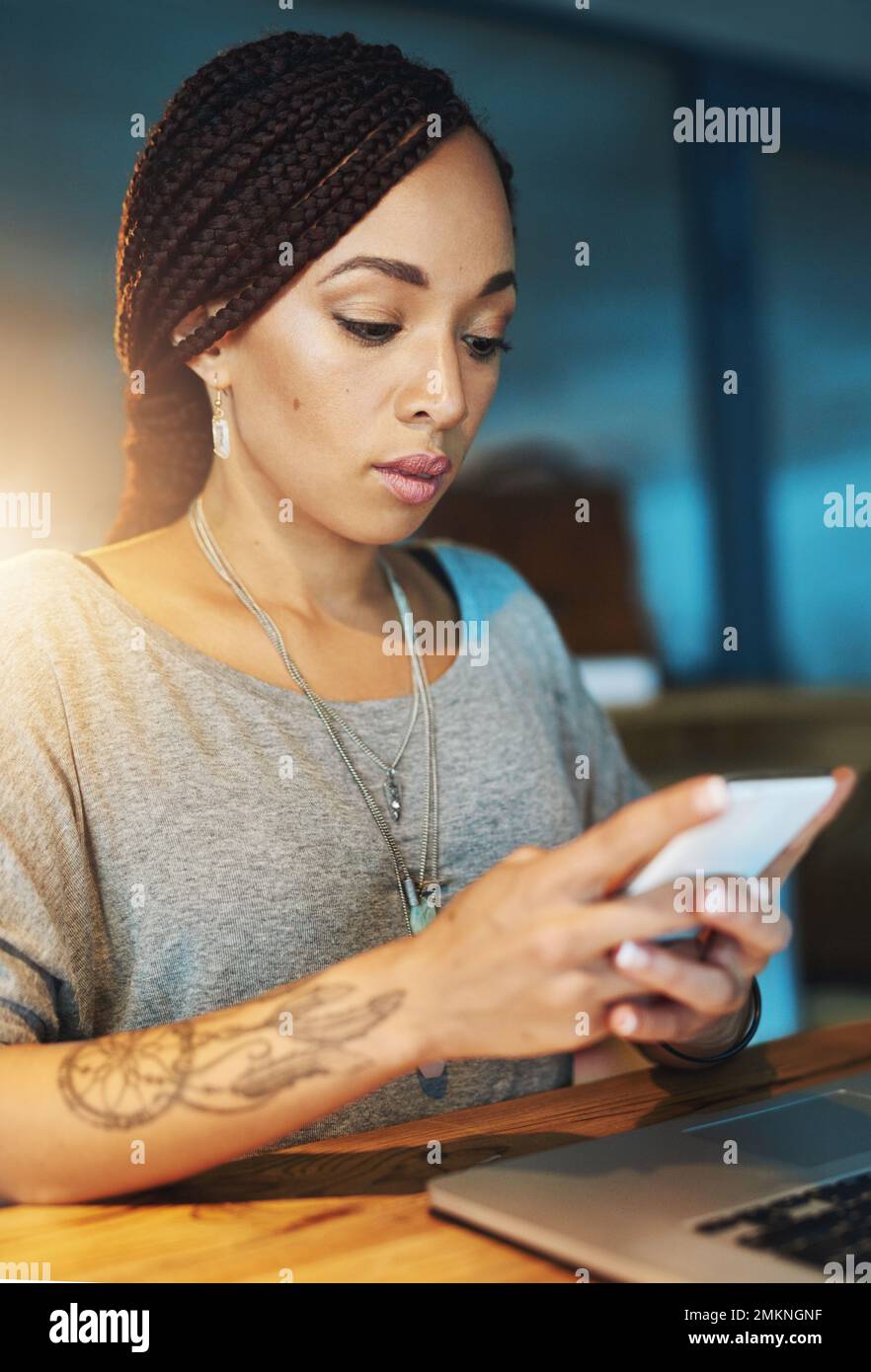 Controllare il suo programma sul suo cellulare. una giovane donna che invia un sms mentre lavora tardi nel suo ufficio. Foto Stock