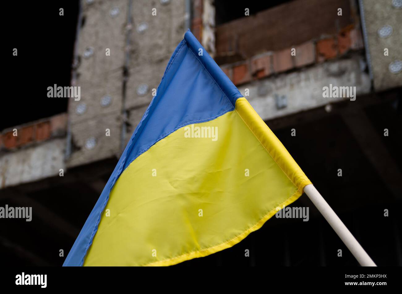 Bandiera nazionale dell'Ucraina di fronte alla casa abbandonata distrutta edificio. Banner ucraino blu e giallo sul sito rovinato distruzione bomba. Foto Stock