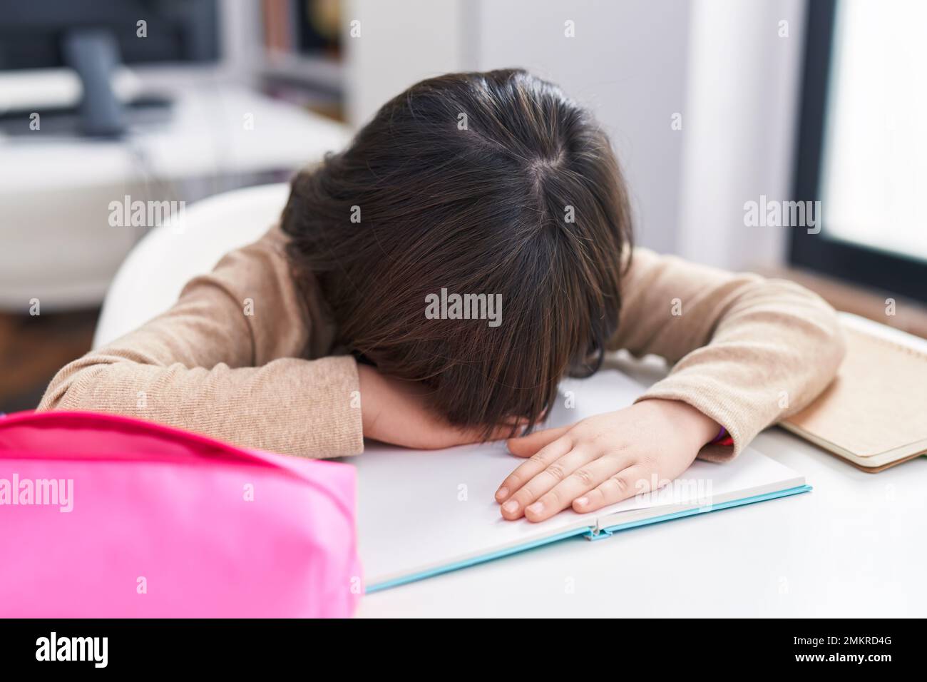 Adorabile ragazza ispanica studente stressato appoggiarsi sul libro in classe Foto Stock