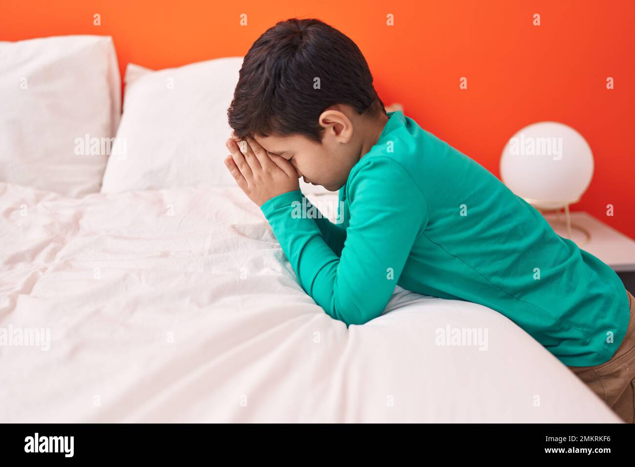 Adorabile ragazzo ispanico seduto sul pavimento in preghiera in camera da letto Foto Stock