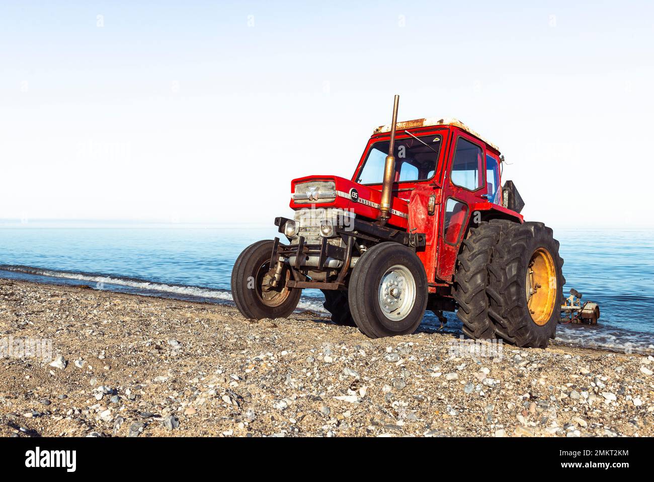 Un vecchio trattore MF 135 Massey-Ferguson rosso è dotato di un rimorchio per imbarcazioni vuoto sulla spiaggia sabbiosa sulla riva di Kattegatt, Djursland, Jutland, Danimarca Foto Stock