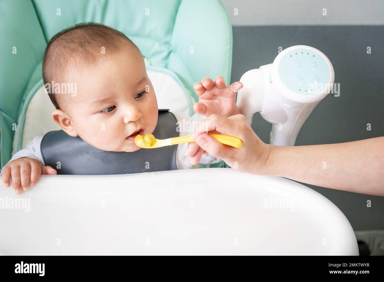 La mamma nutre il bambino con un cucchiaio di purea di verdure al tavolo per l'allattamento dei bambini. Appetito del bambino, nutrizione sana, introduzione di complementare Foto Stock