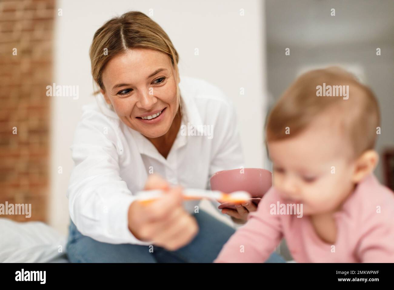 Nutrizione del bambino. Madre felice che alimenta la ragazza cute del bambino dal cucchiaio, mamma premurosa che dà il cibo sano a sua figlia nel paese Foto Stock