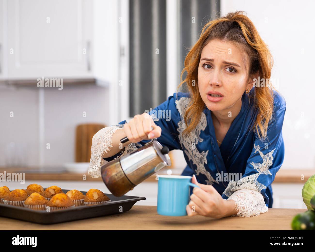 Donna addormentata in housecoat bere il caffè del mattino in cucina Foto Stock