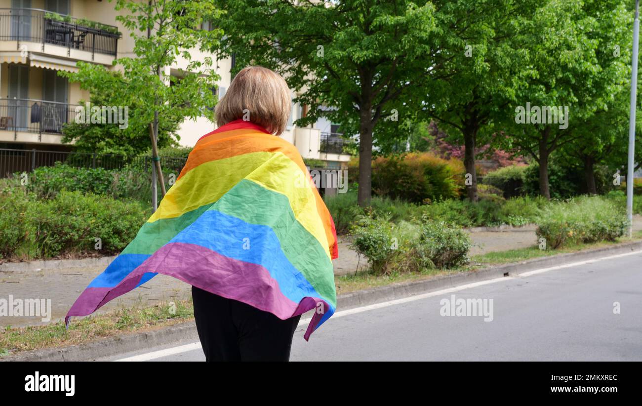 Bisessuale, lesbica, donna, transgender si erge con bandiera LGBT contro il cielo blu con le nuvole in una giornata di sole e celebrare bisessualità giorno o Nazionale Coming out Day Foto Stock