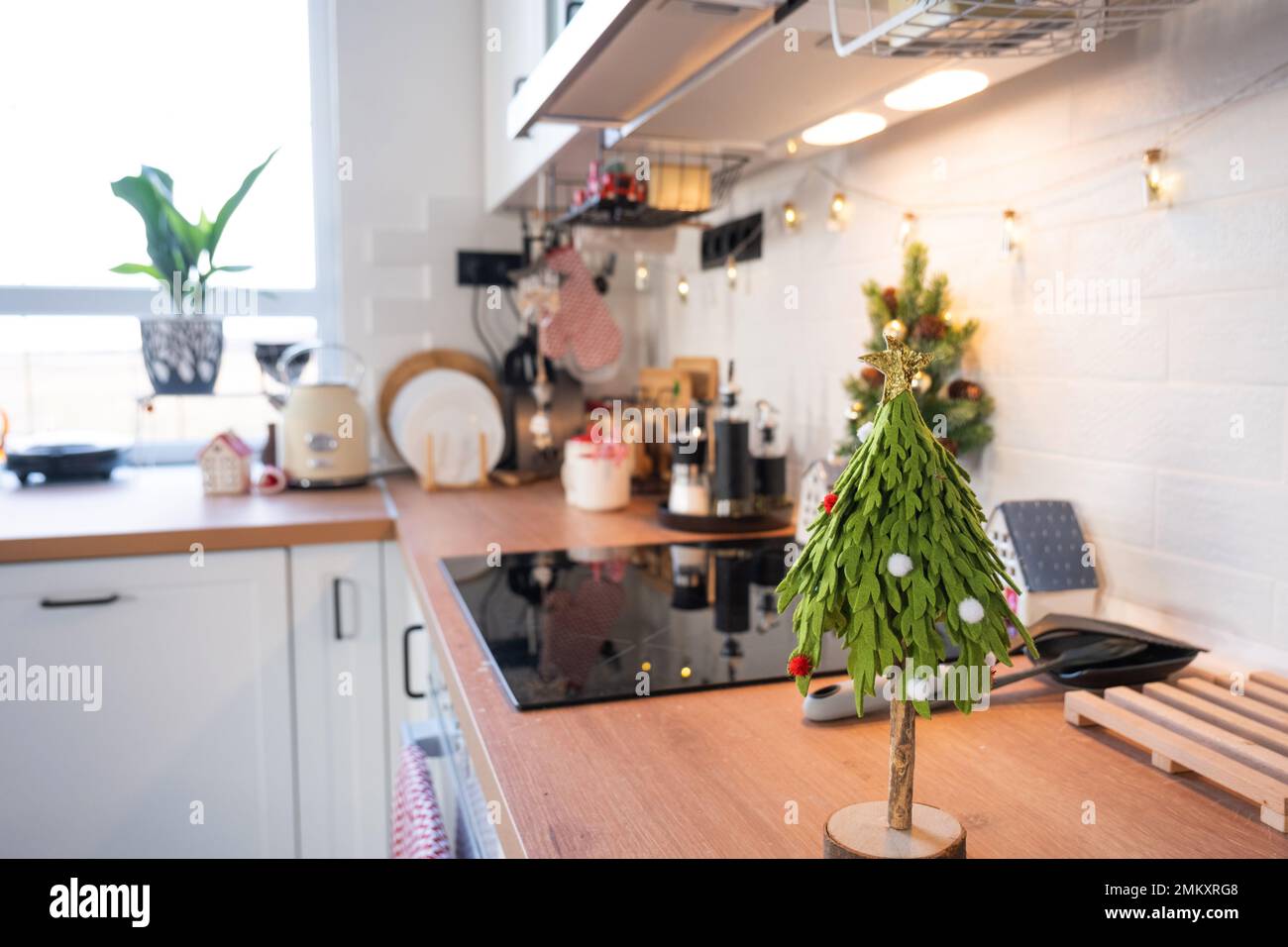 Decorazione della cucina di Natale - preparazione per una vacanza in famiglia, luce fata, albero di Natale, ornamento rosso, cervo divertente su armadi, stufa. Umore del celebrato Foto Stock