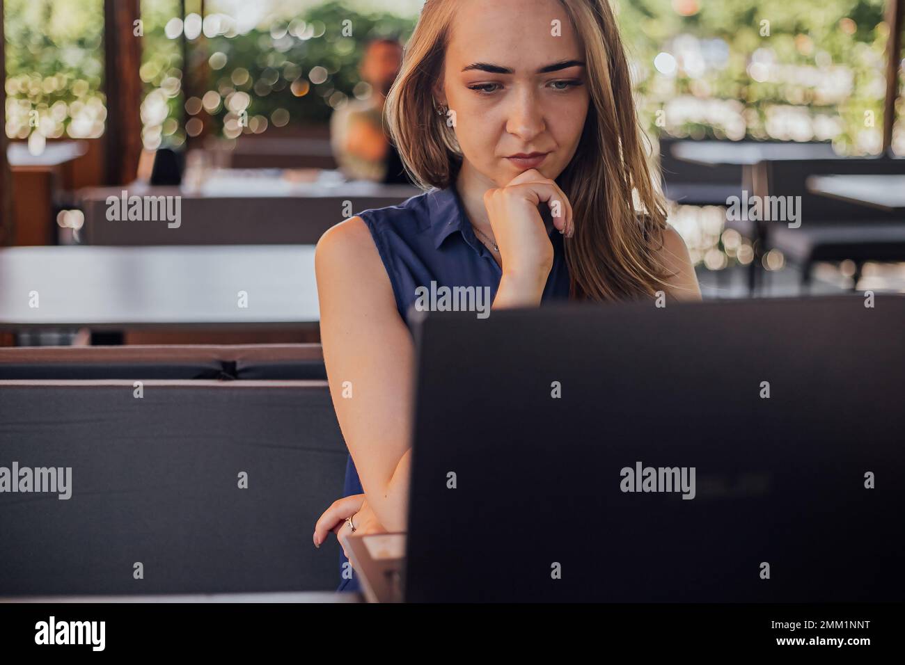 una ragazza si siede su una terrazza estiva e lavora su un computer portatile. freelance. autofiduzione. il concetto di apprendimento remoto e di lavoro all'aperto Foto Stock