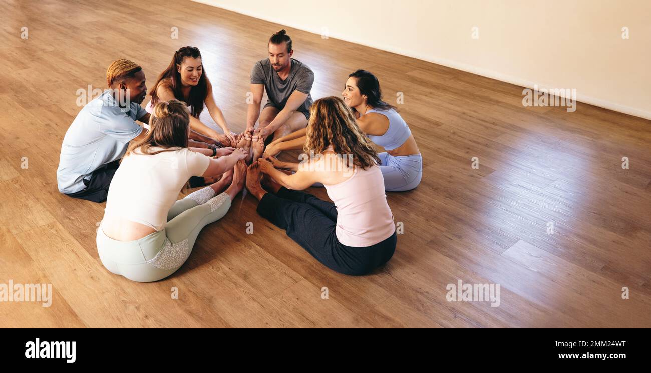 Gente felice che fa la testa a posa di yoga del ginocchio mentre siede insieme in un cerchio. Gruppo di persone multiculturali che fanno esercizi di stretching durante un yo Foto Stock