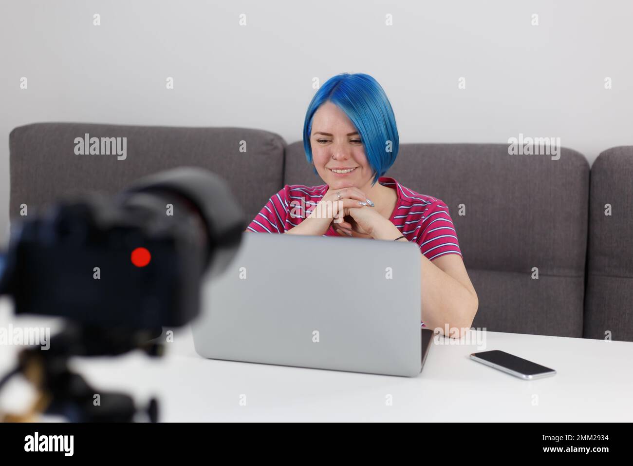 Allegro video blogger donna con tinto capelli blu parla su fotocamera professionale su treppiede. Video del blog dei film in linea dell'allenatore nel paese Foto Stock