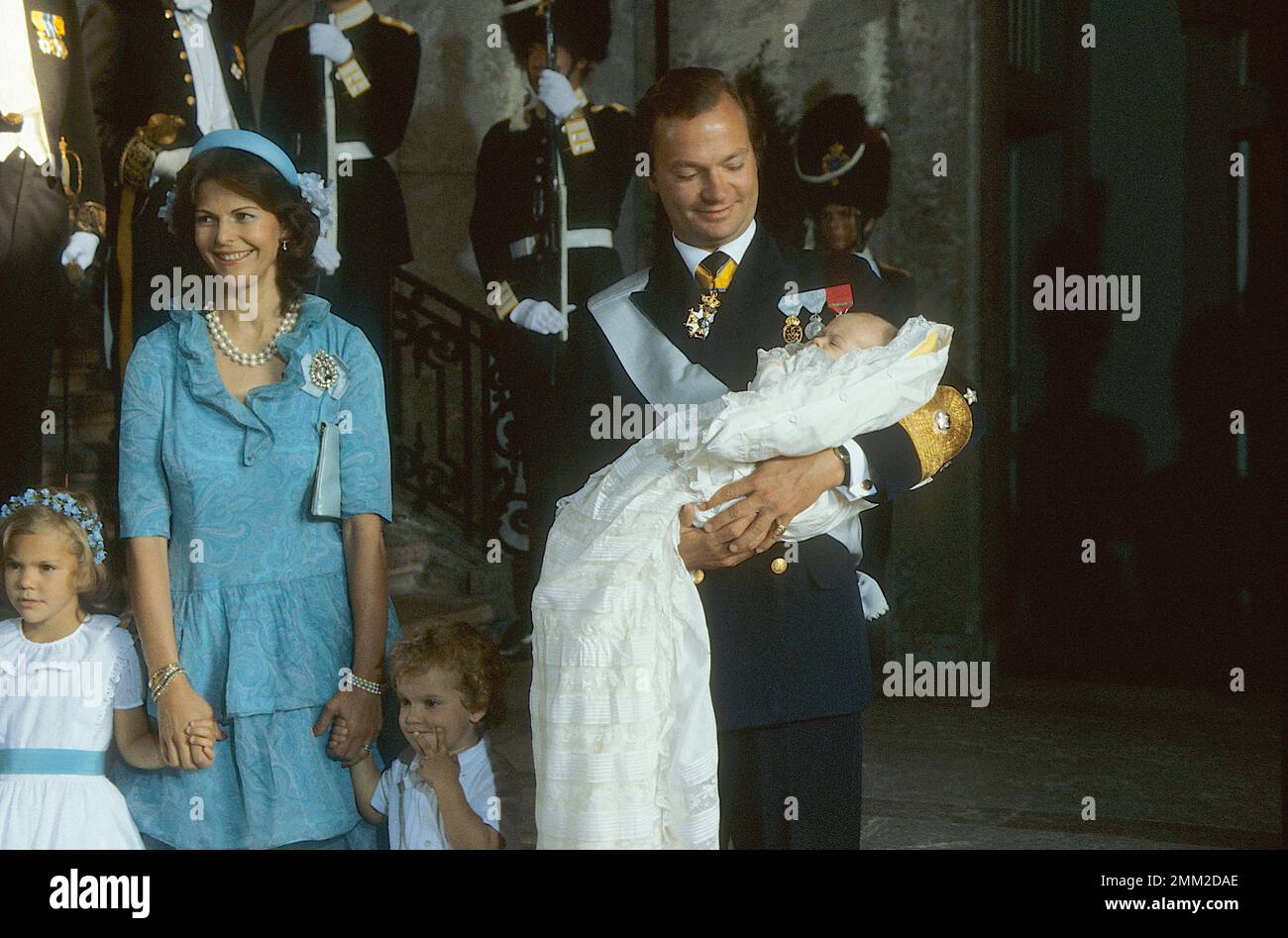 Carl XVI Gustaf, re di Svezia. Nato il 30 aprile 1946. Il re Carlo XVI Gustaf tiene la principessa Madeleine durante il battesimo di lei a Slottskyrkan Stoccolma 31 agosto 1982. La principessa della corona Victoria, la regina Silvia e il principe Carl Philip. Foto Stock