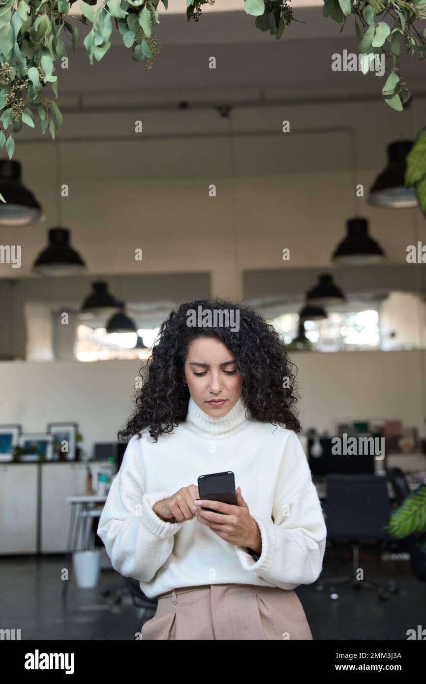 Giovane donna business latina che utilizza un telefono cellulare in ufficio, verticale. Foto Stock