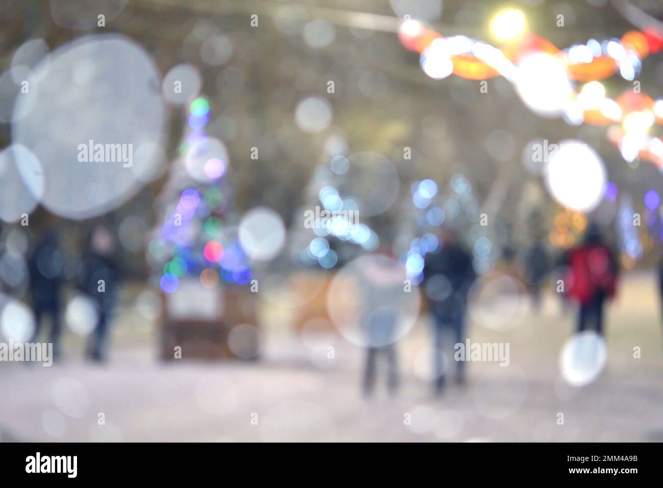 Sfondo sfocato astratto. Persone che camminano per strada di alberi di Natale decorati con illuminazione luminosa, luci incandescenti e ghirlande in città durante le pesanti nevicate nella notte d'inverno Foto Stock