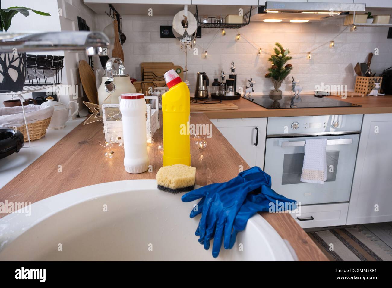 Pulizia della cucina prima delle vacanze di Natale e Capodanno. Detersivo, polvere secca, spugna, guanti sono sul lavello. Decorazioni natalizie nella divisa bianca Foto Stock