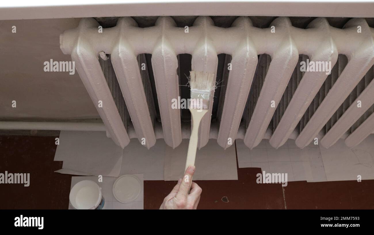verniciatura in smalto bianco di un radiatore di riscaldamento retroriflesso con spazzola a manico lungo per accedere ai punti difficili da raggiungere, vista dall'alto Foto Stock