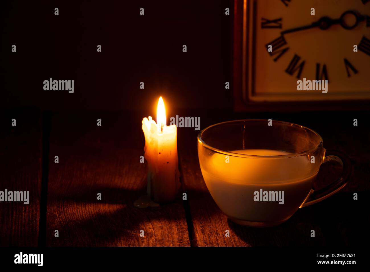 candela fiamma e tazza con latte su un tavolo in una stanza buia Foto Stock