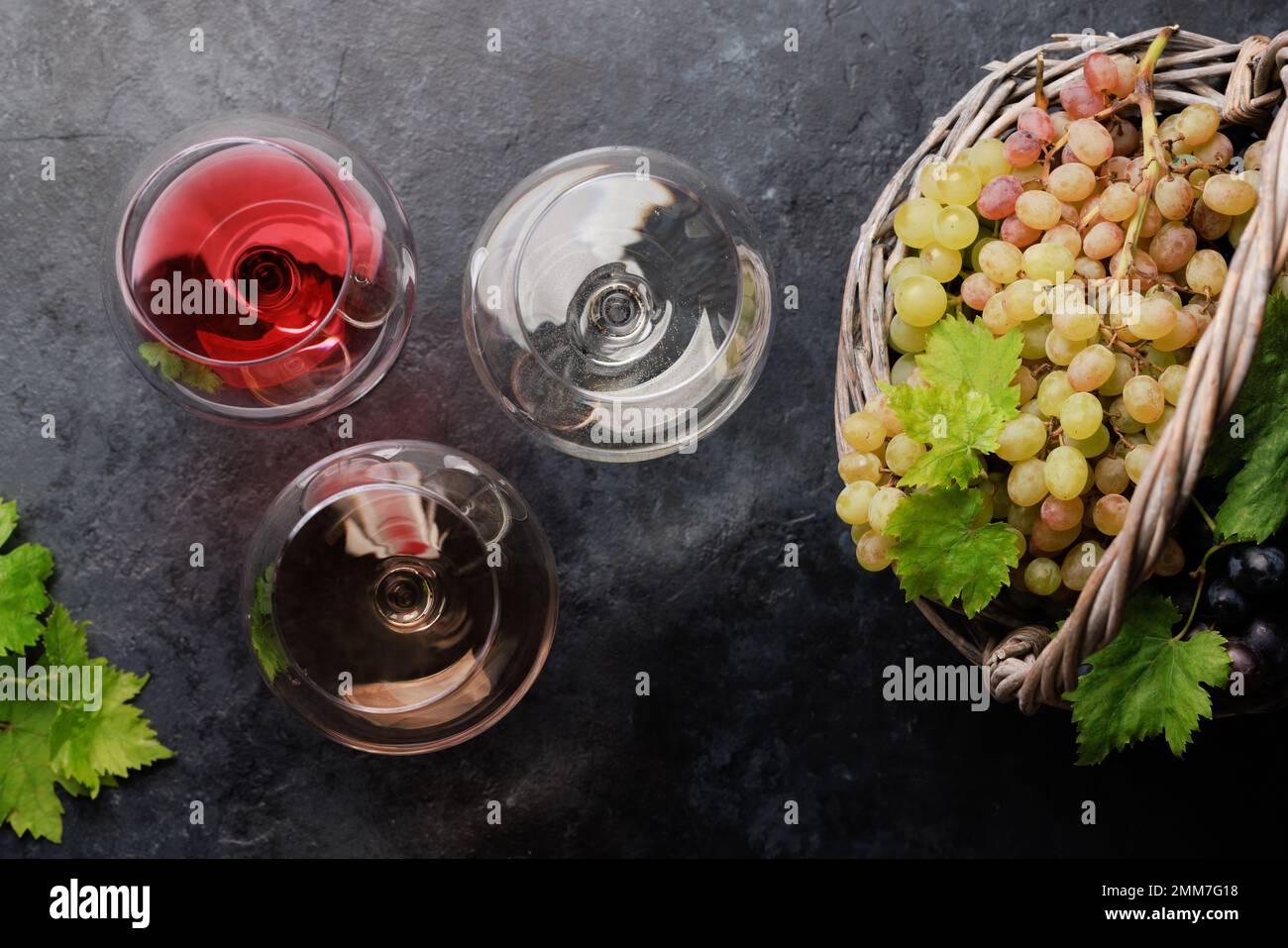 Bicchieri da vino bianco, rosato e rosso e uva in cesto. Giacitura piatta Foto Stock