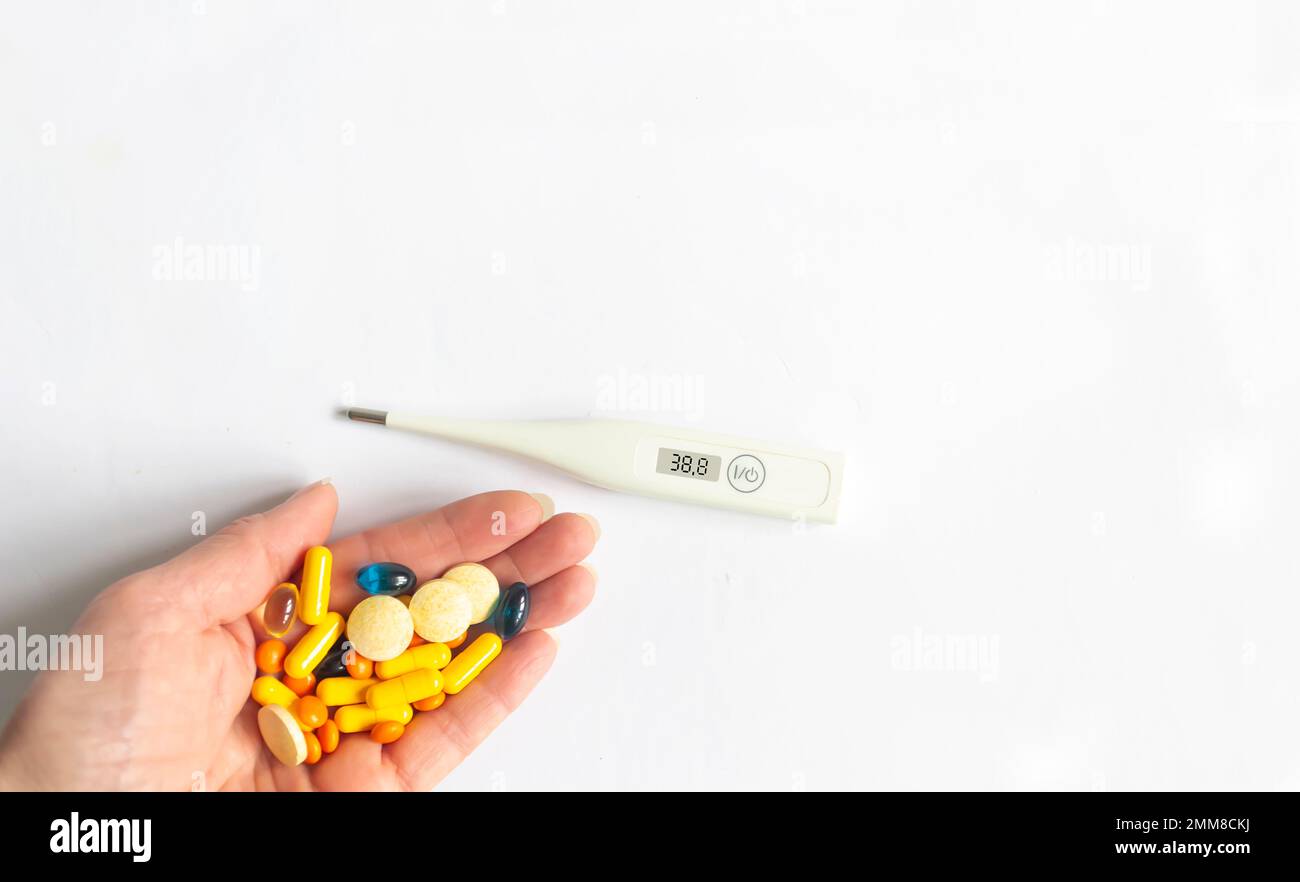 Termometro elettronico e pillole a portata di mano su sfondo bianco Foto Stock