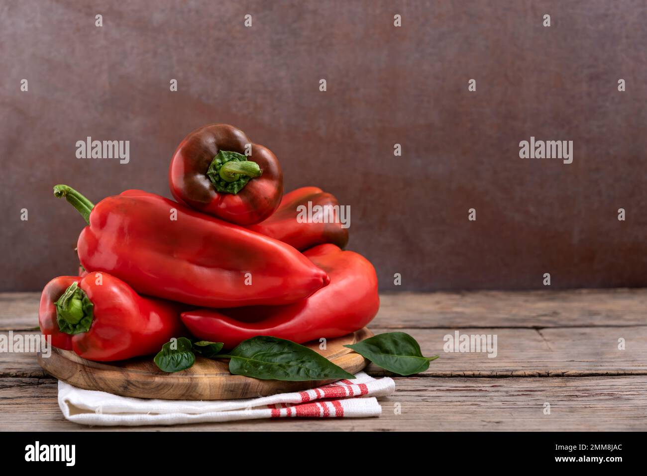 Taglieri con peperoni rossi dolci e foglie verdi su tavola di legno. Messa a fuoco selettiva. Foto Stock