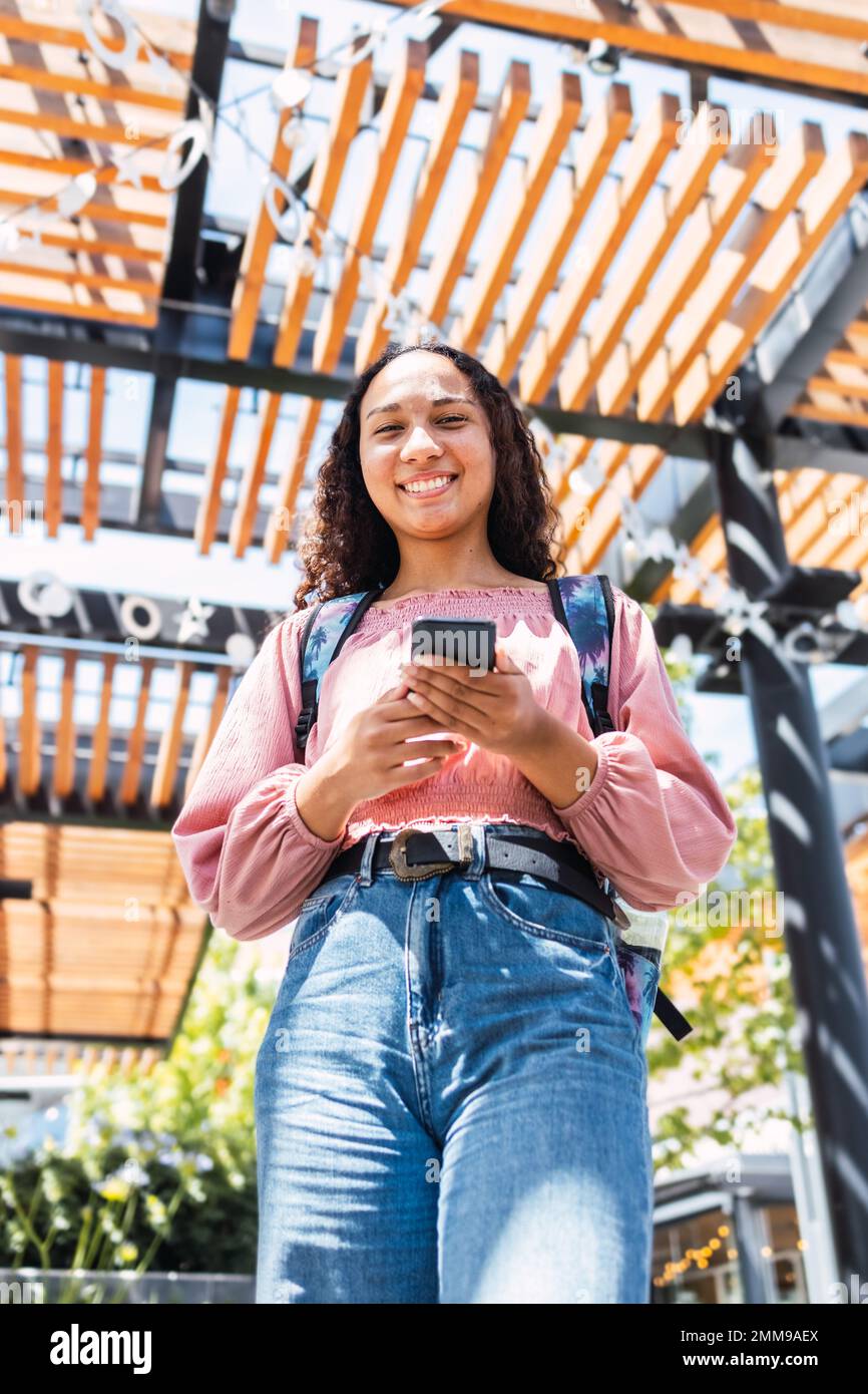 Studentessa universitaria latina sorridente e con il suo smartphone. Guardando la fotocamera Foto Stock