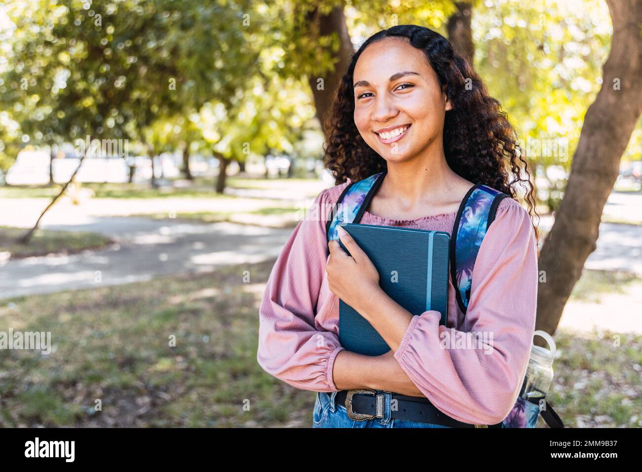 Girovita su scatto di una giovane studentessa latina che tiene i suoi libri nel parco. Fiducia in se stessi Foto Stock