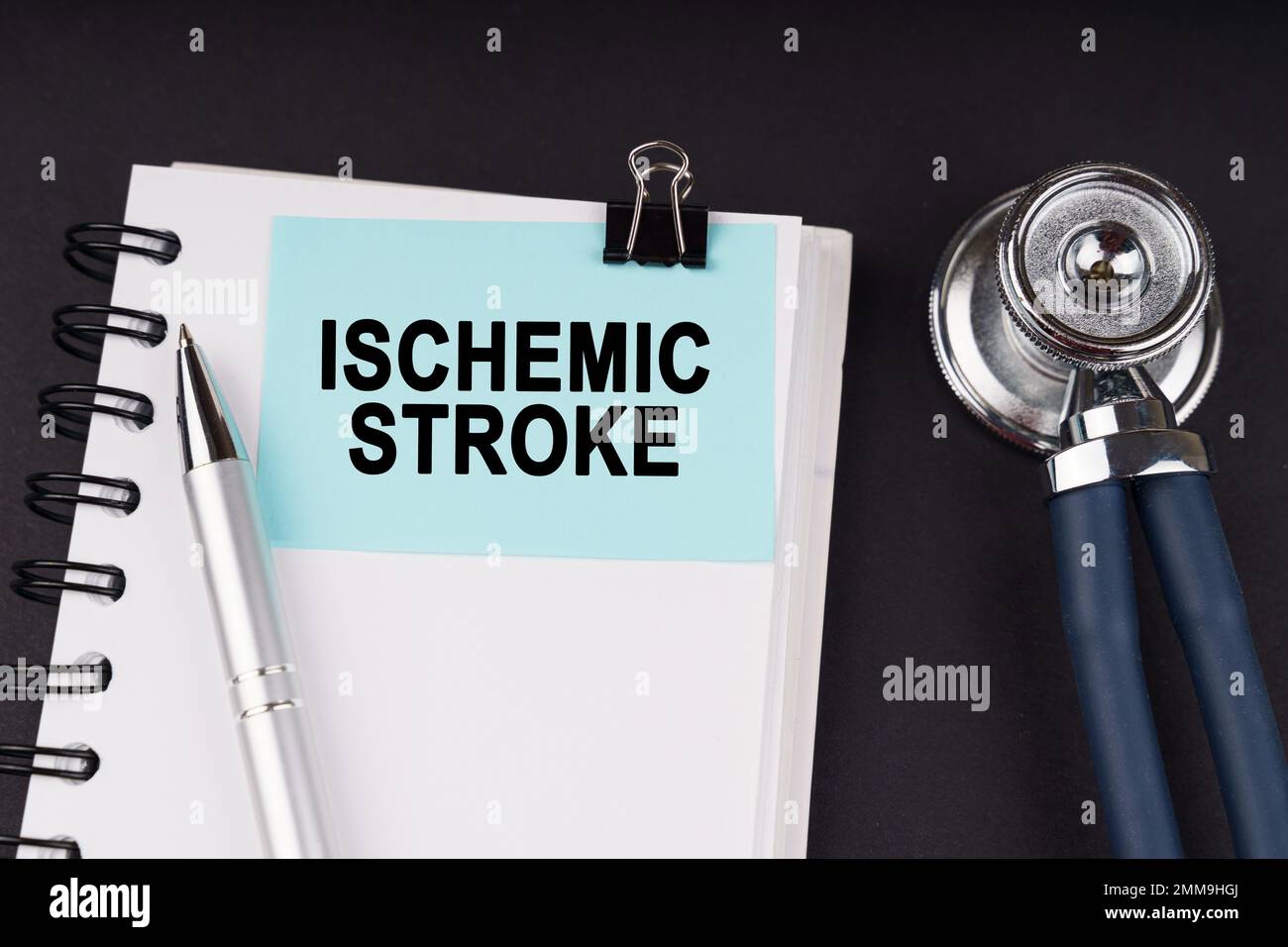 Concetto medico. Su una superficie nera, uno stetoscopio, un taccuino, una penna e un adesivo blu con l'iscrizione - ICTUS ISCHEMICO Foto Stock