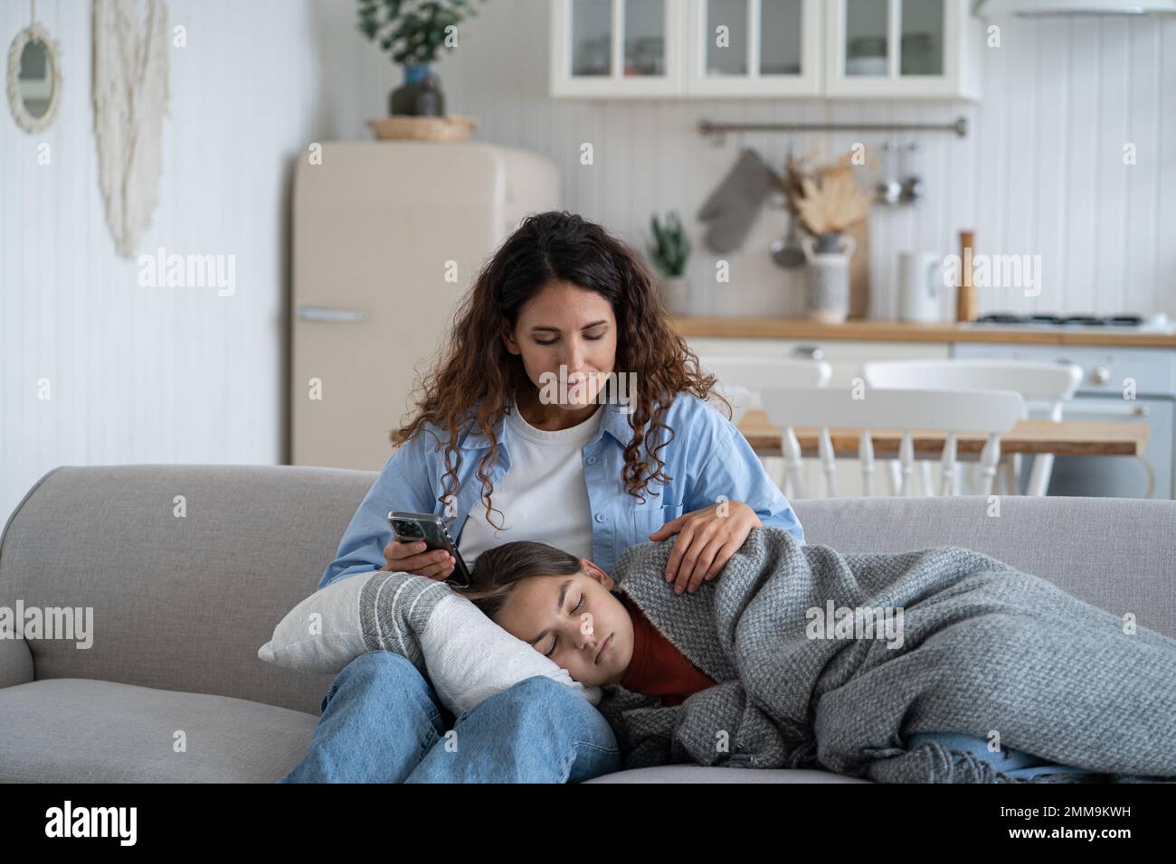 Amorevole donna sorride si siede sul divano nel soggiorno e guardando la figlia che si addormenta sulle ginocchia Foto Stock