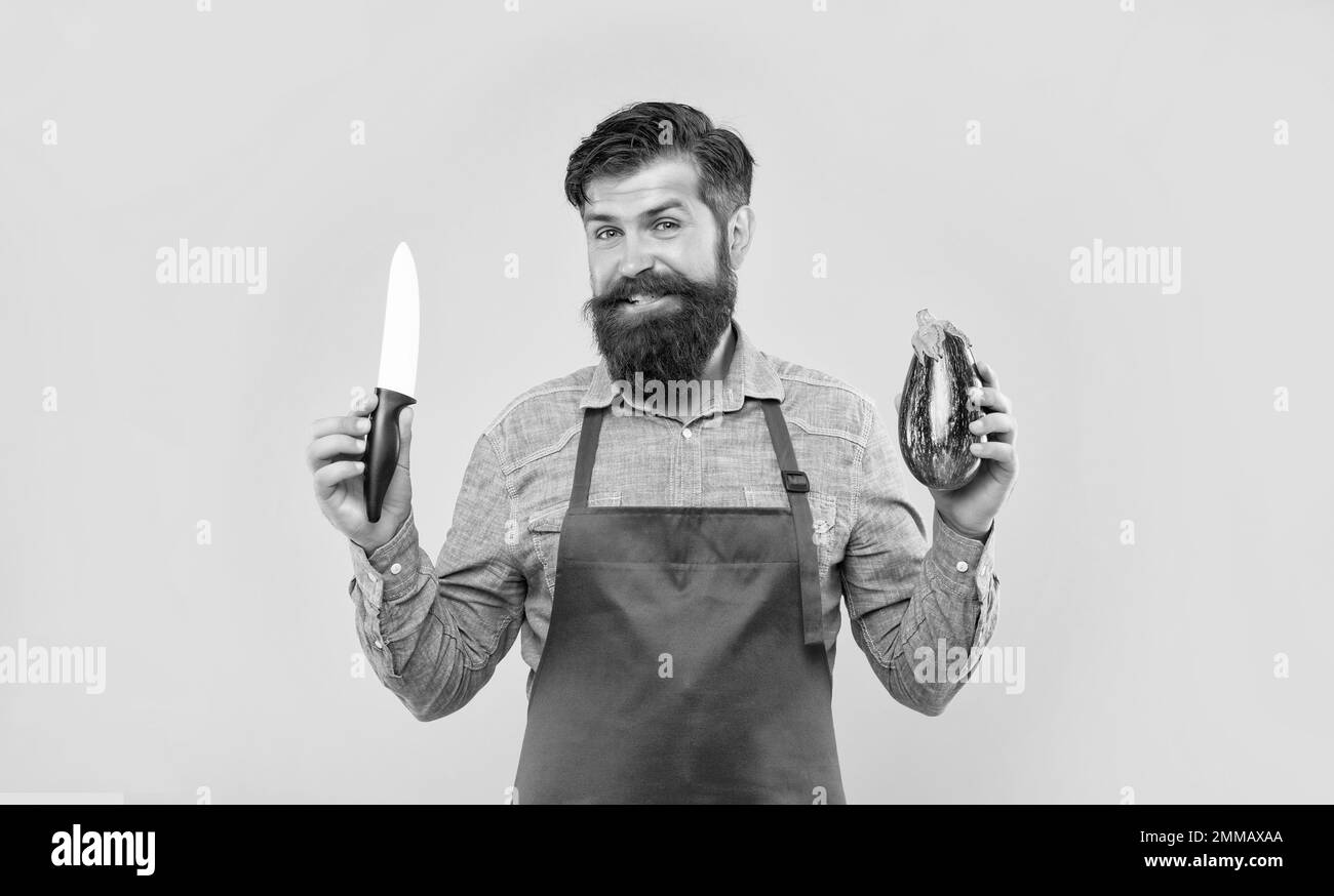 Uomo felice in grembiule tenendo chef coltello e melanzane sfondo giallo, chef Foto Stock