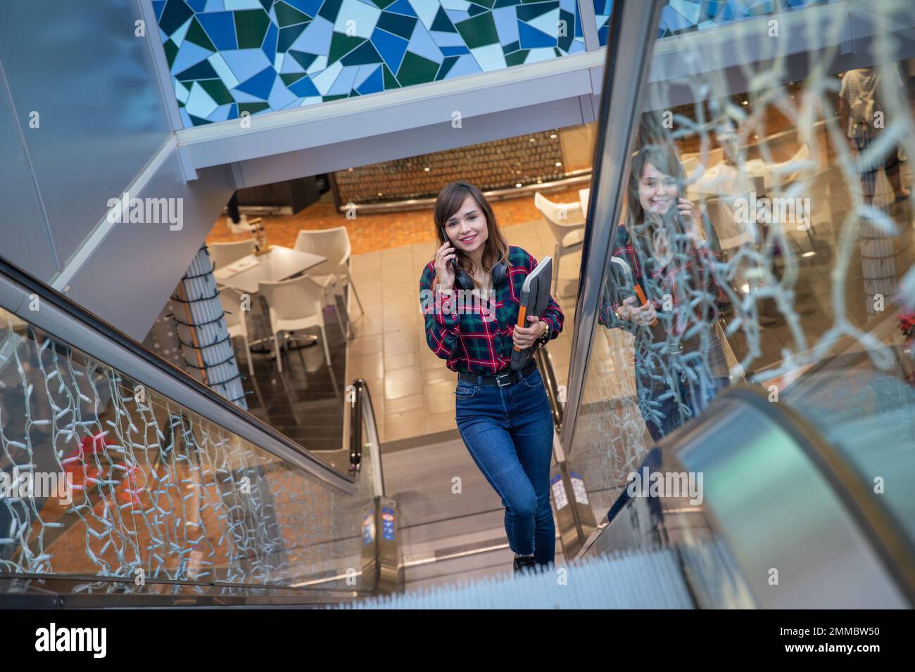 Una donna effettua una chiamata mentre usa la scala mobile in un centro commerciale Foto Stock