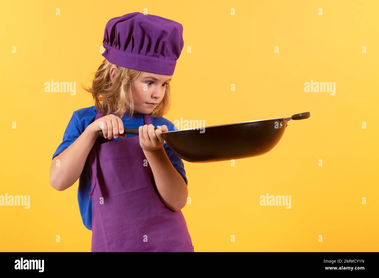 Cuoco per bambini con pentola. Cucina per bambini, il piccolo chef prepara il cibo. Bambino in cappello e grembiule chef su sfondo giallo isolato studio. Foto Stock