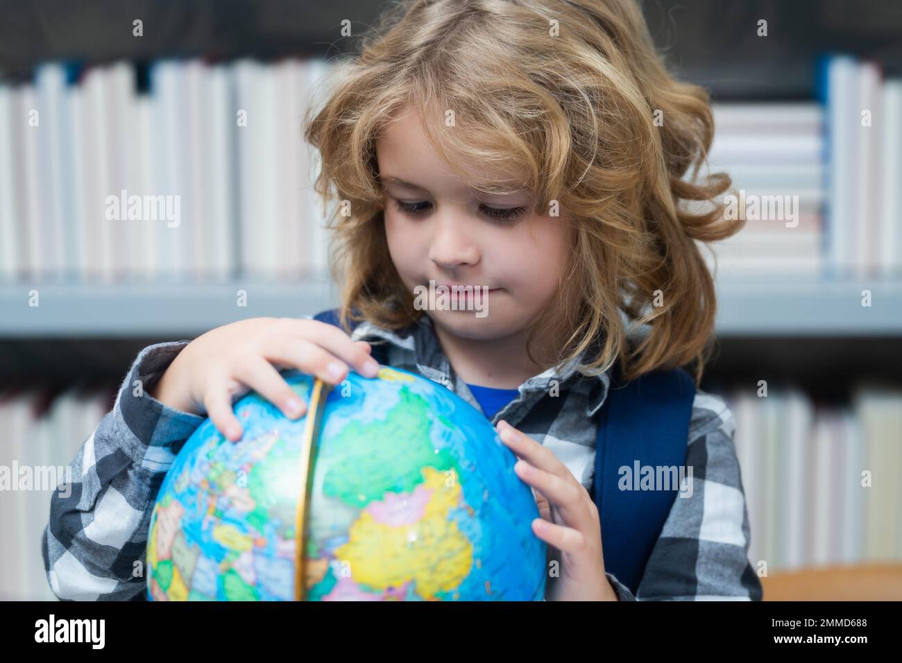 Allievo che guarda il globo in biblioteca alla scuola elementare. Bambino della scuola nerd. Bambino intelligente della scuola elementare con libro. Intelligenza geniale intelligente Foto Stock