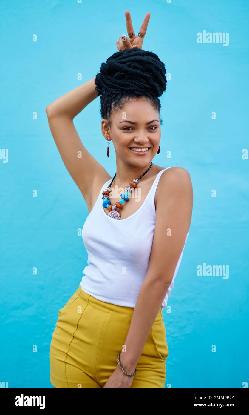 Personalità e stile affascinanti da abbinare. Ritratto di una giovane donna alla moda che fa un gesto coniglietto orecchie su sfondo blu. Foto Stock