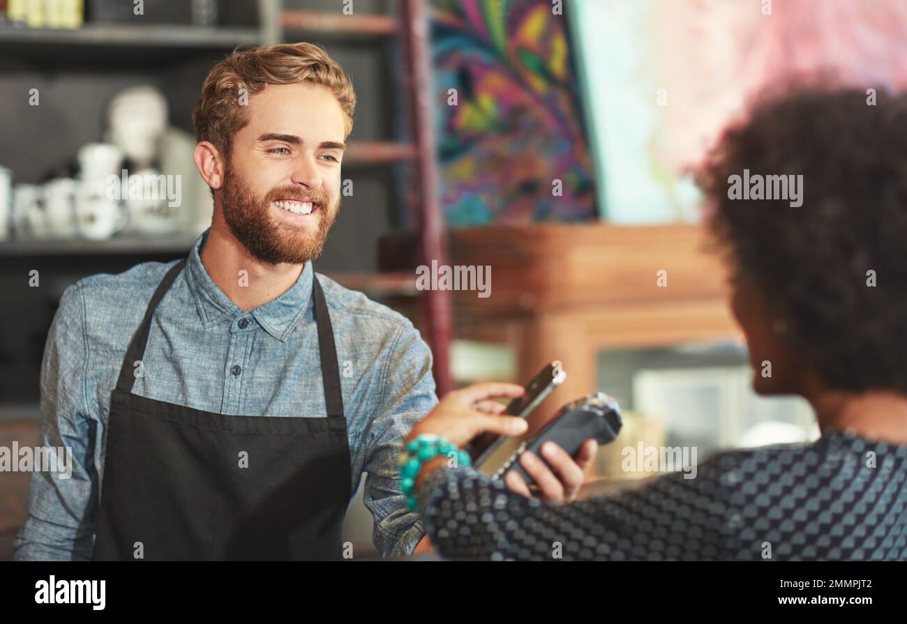 Transazioni senza carta, l'unico modo per pagare. un barista che prende un pagamento tramite smartphone da un cliente in un bar. Foto Stock